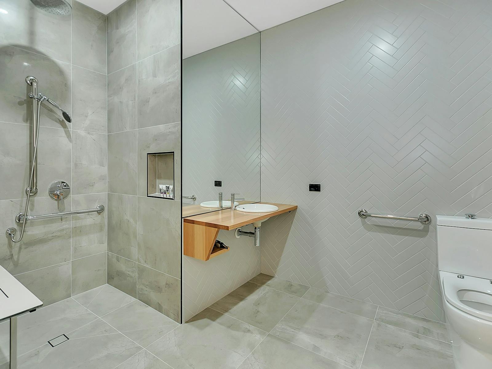 Accessible bathroom, with large shower with no door or curtain, accessible low basin and toilet.