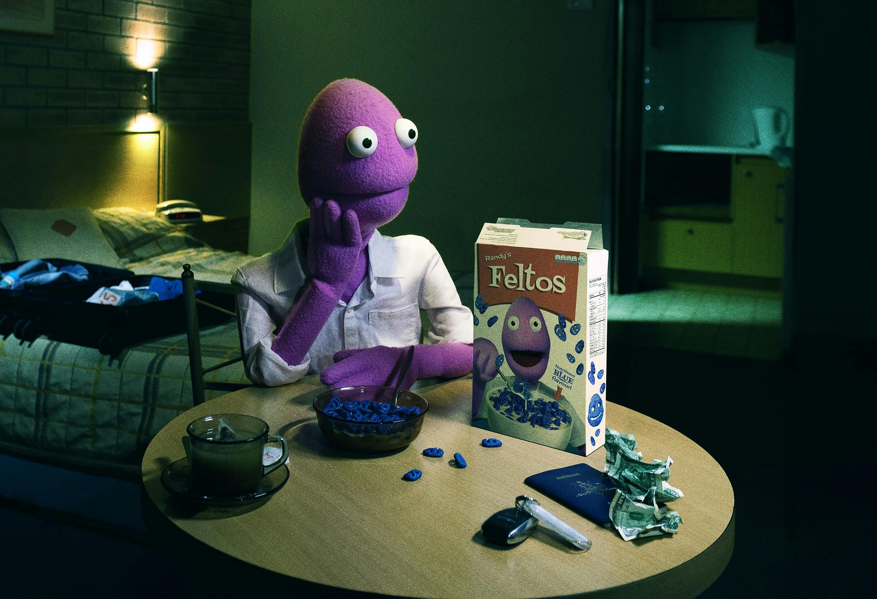 Randy Feltface puppet sitting at a dining table with a bowl of cereal labelled 'Feltos'