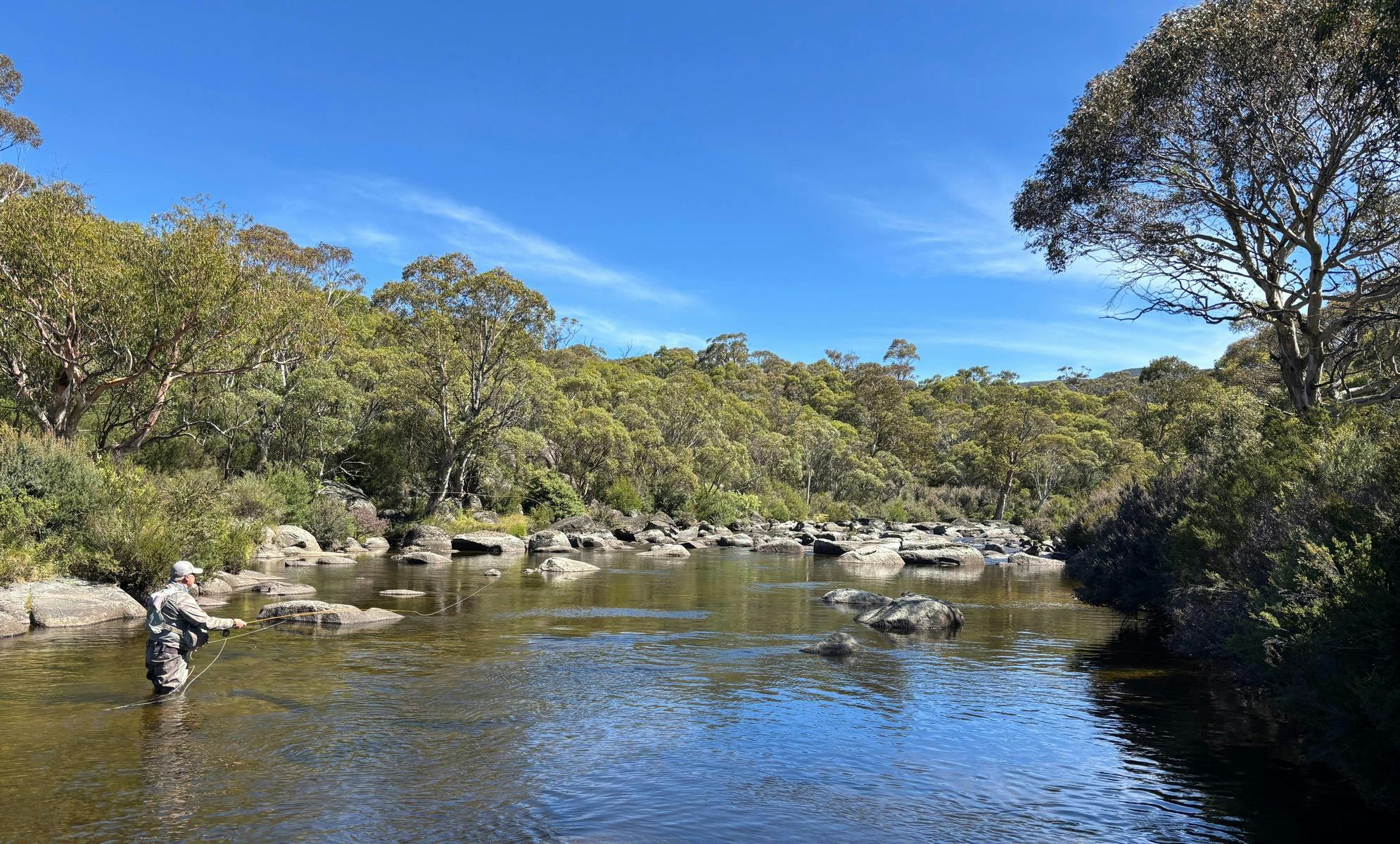 A fisherman casting his fly fishing rod up the river