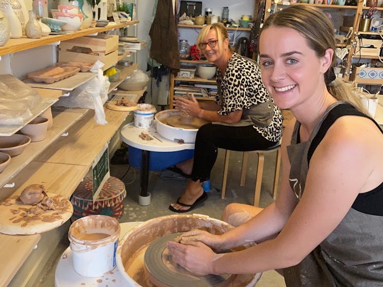 picture shows two women smiling sitting at pottery wheel