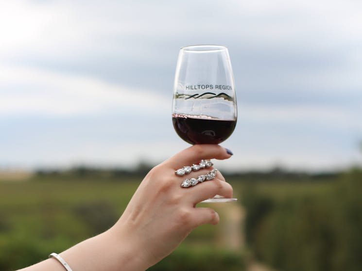 Hand holding glass of red wine with Hilltops Region logo