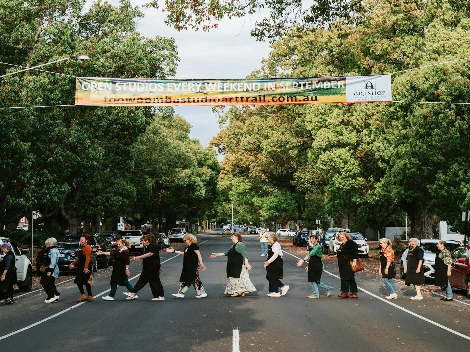 A line of artists walking underneath a large street banner