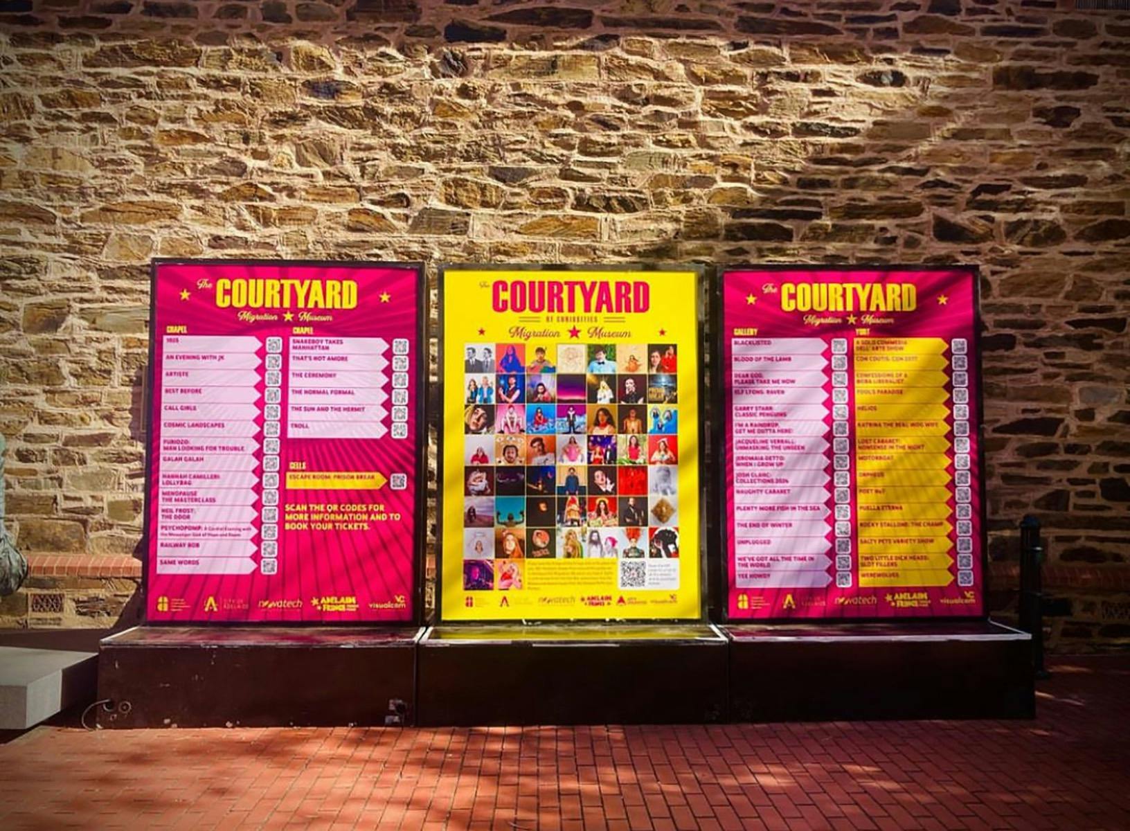 Three light boxes in front of a stone building showing information for shows
