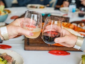 Two BCF wine tumblers - one white, one red - cheersing in front of table of food in background.