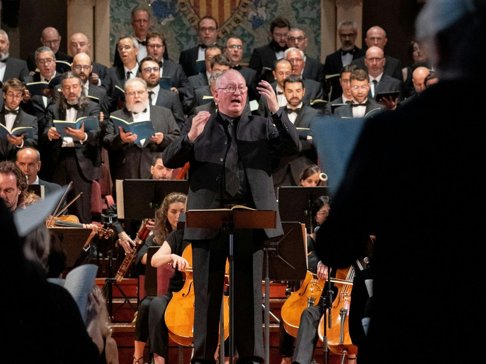 Conductor in formal attire passionately leading a choir and orchestra during a performance