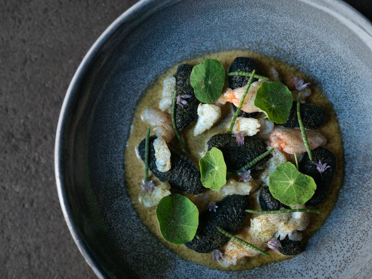 A dish of hand rolled squid ink gnocchi, crab, lobster bisque and garden nasturtiums