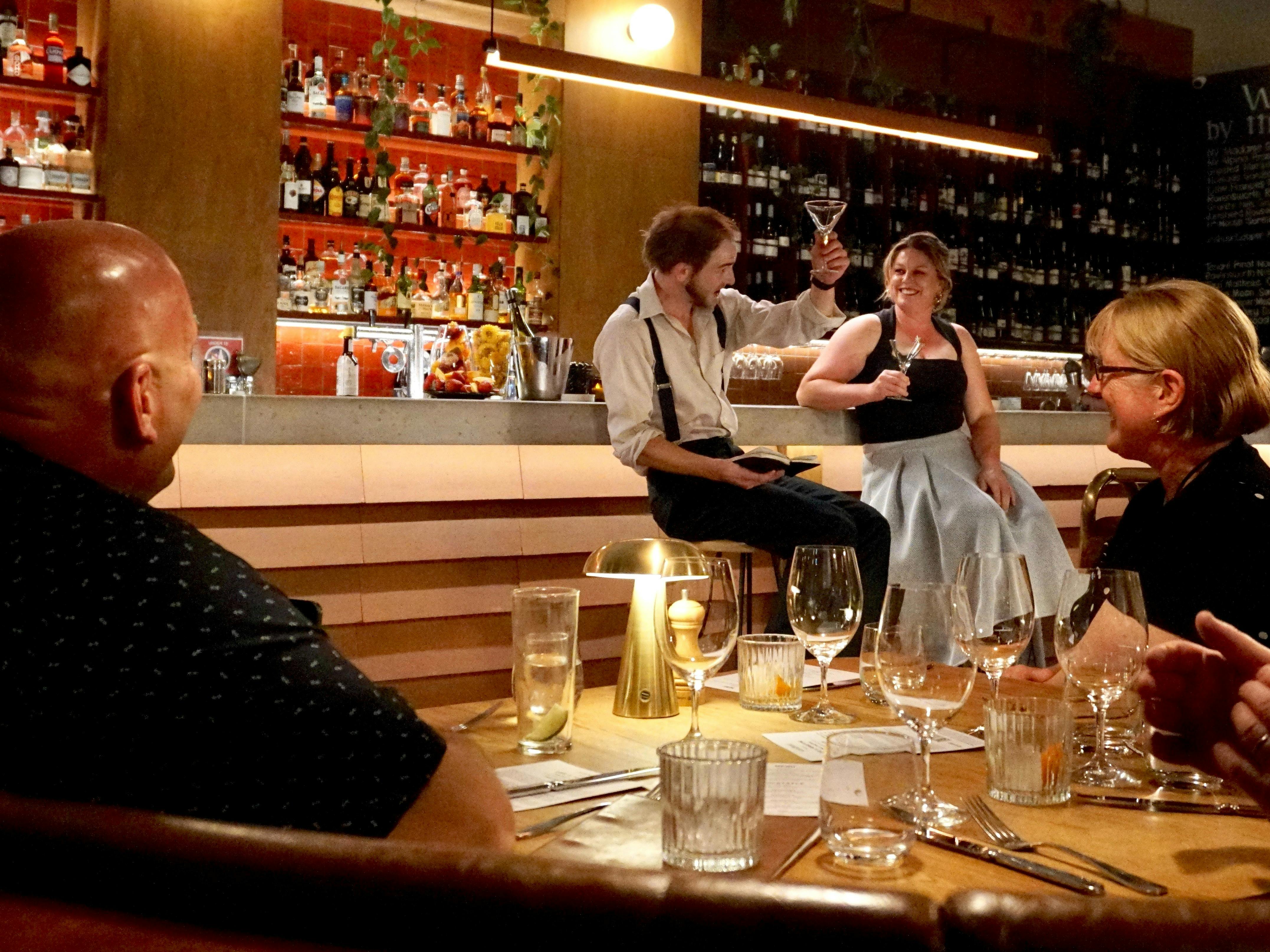 a performing bartender and audience participant raise a glass together at the bar