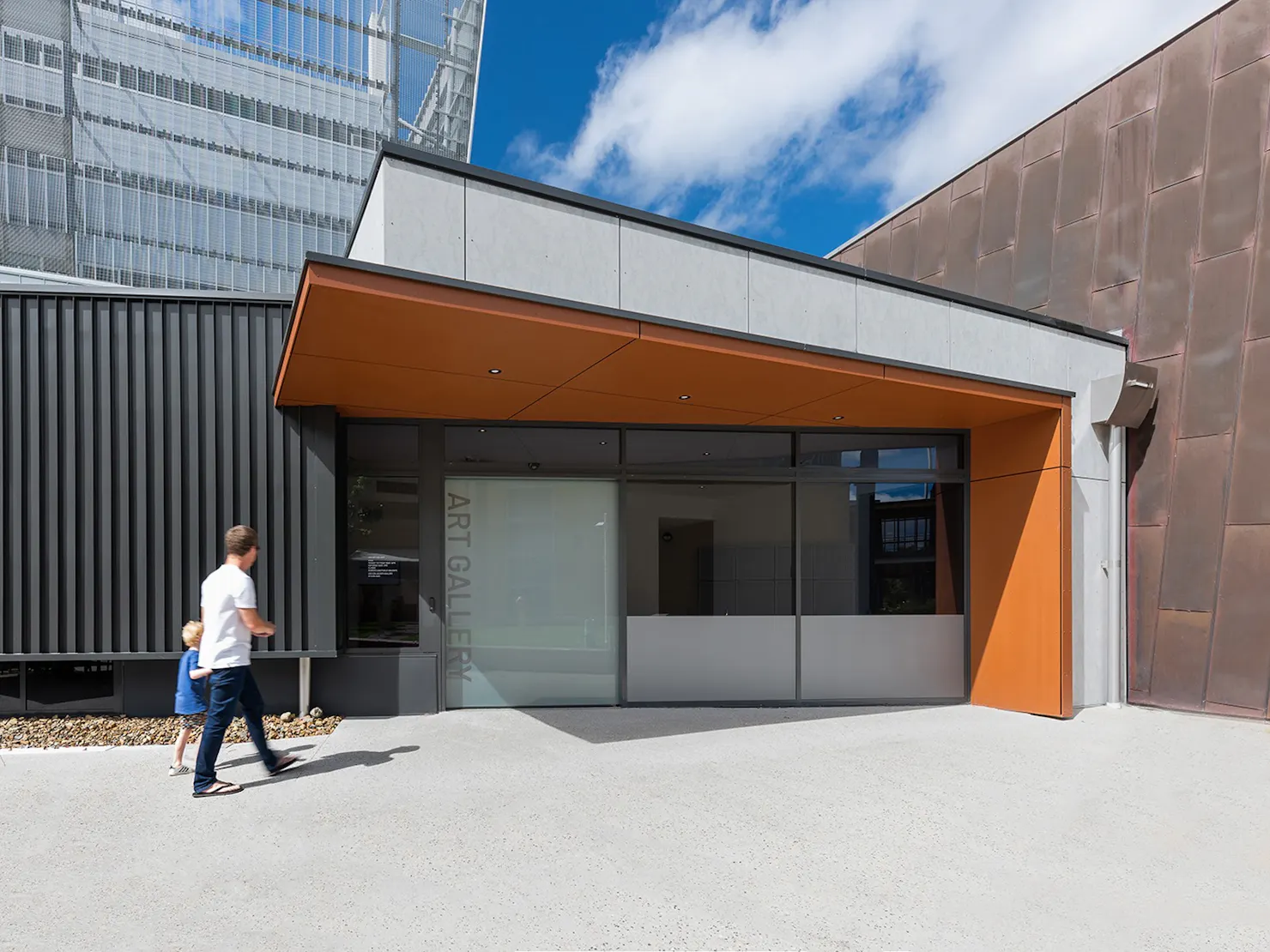 A man and child walking toward the entrance of a modern art gallery with a glass door.