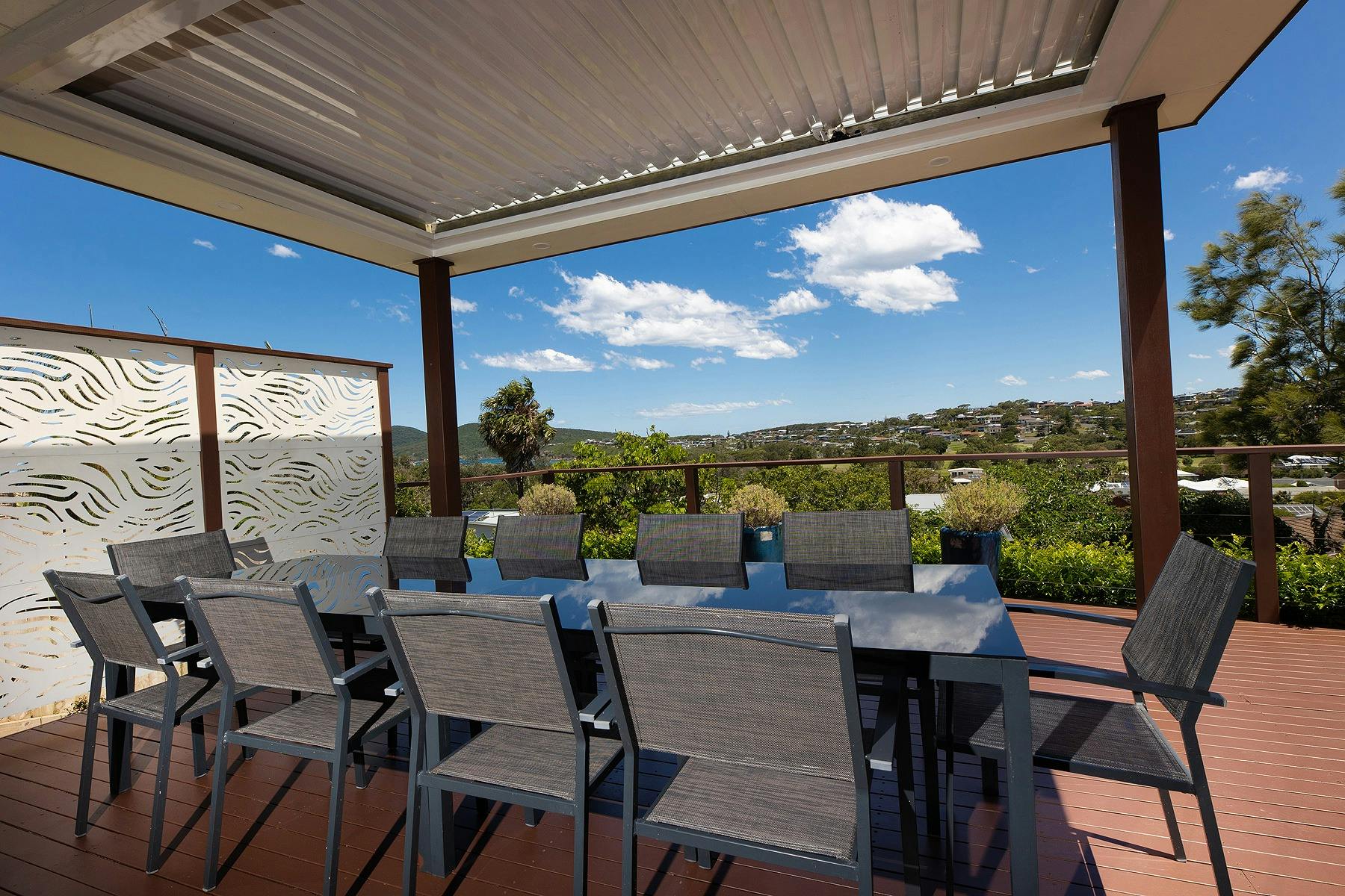Outdoor entertaining deck with views of the coastline, a barbecue and 10 seater dining setting