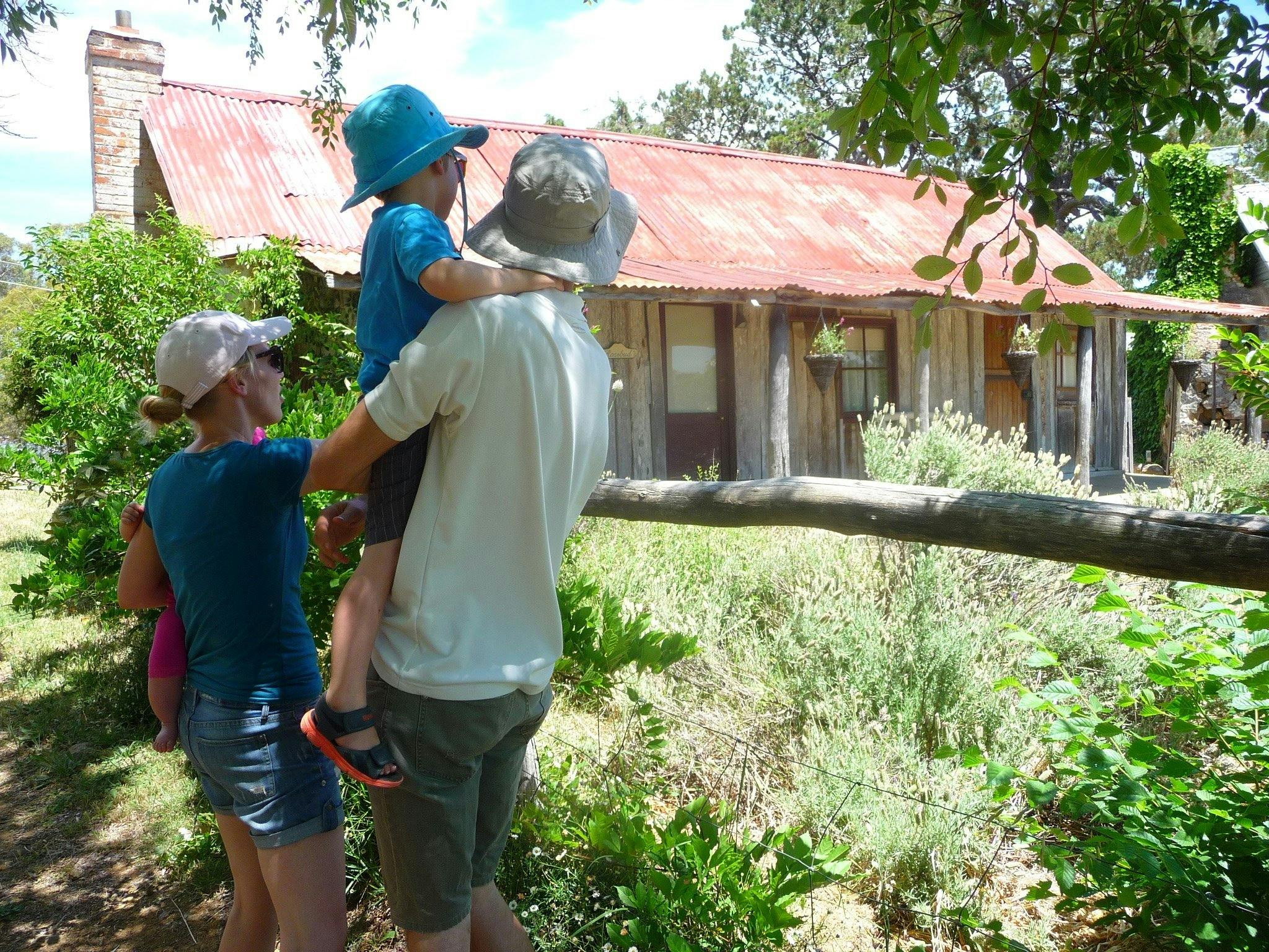 Young family in summer clothes and hats looking at an old wooden hut
