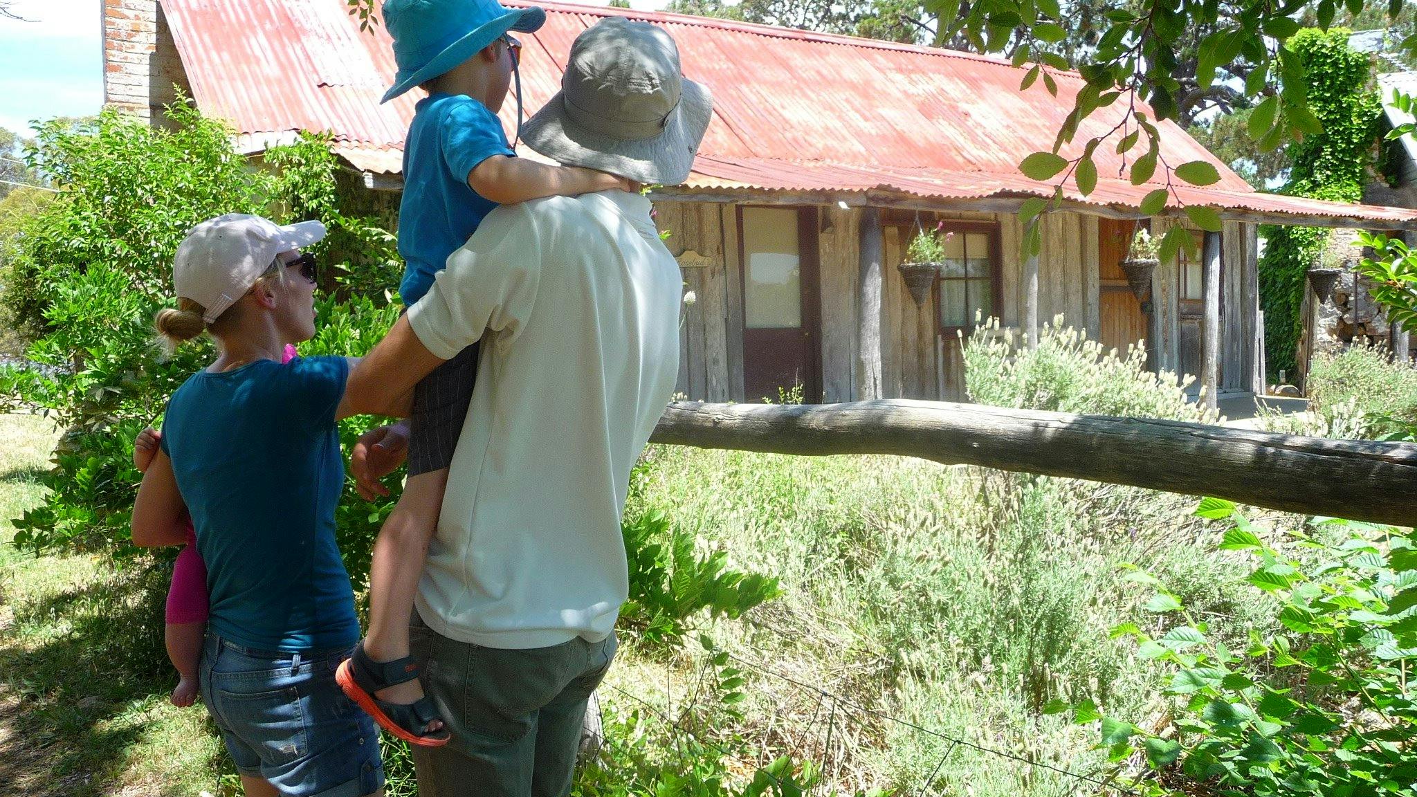 Young family in summer clothes and hats looking at an old wooden hut