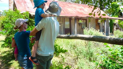 Young family in summer clothes and hats looking at an old wooden hut