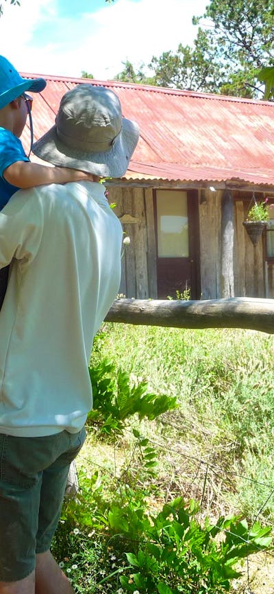 Young family in summer clothes and hats looking at an old wooden hut