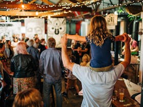 Child sits on adults shoulders dancing to the music as the audience sing