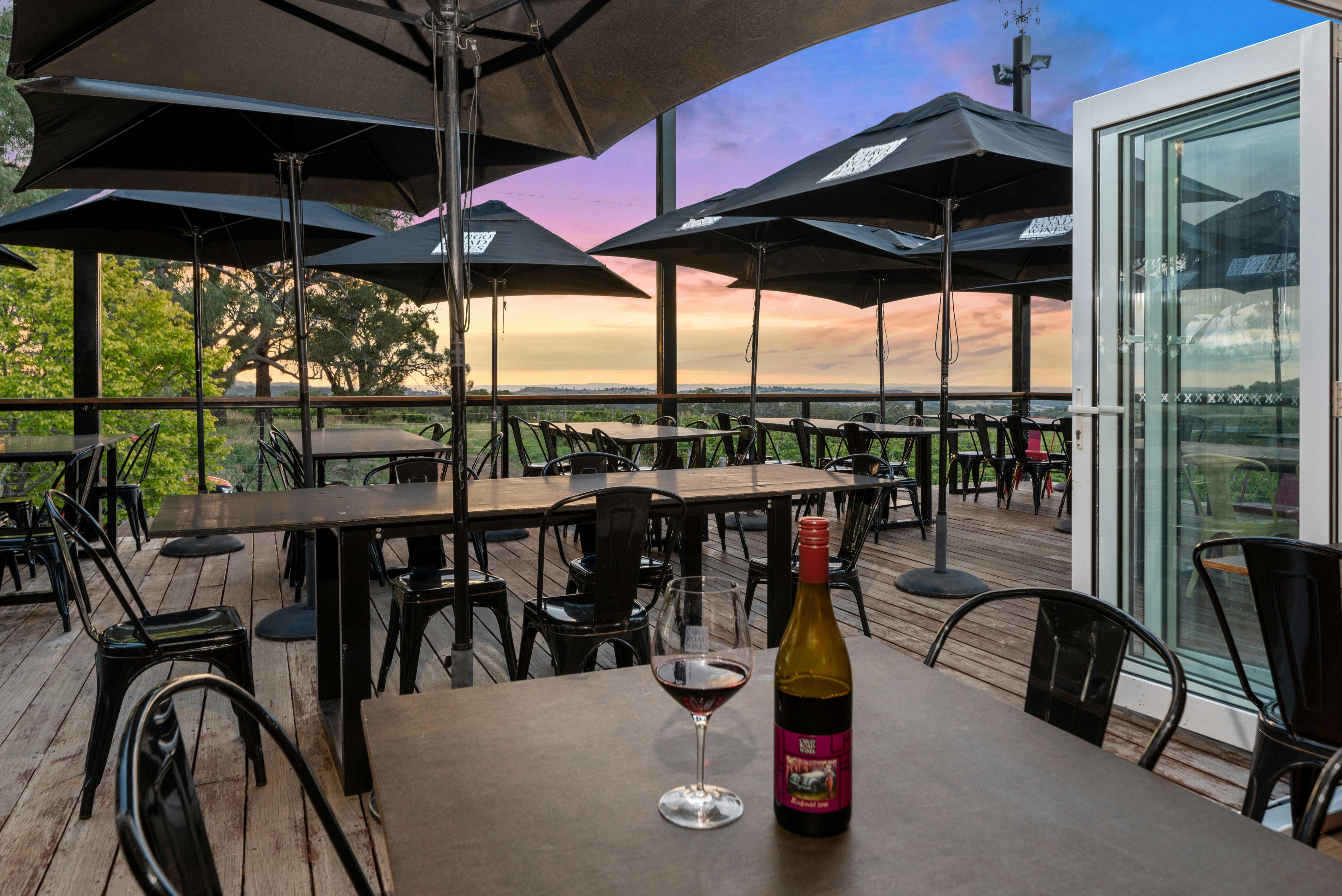 glass of wine and bottle on table overlooking tables and chairs at  sunset