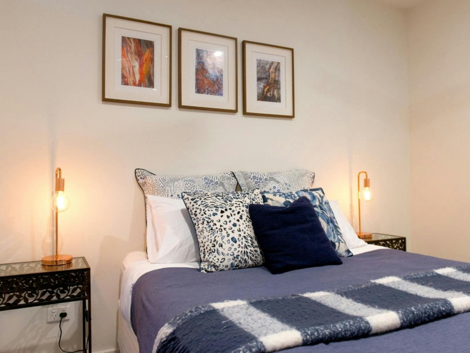 Bedroom two with a bed, three paintings above and side tables either side