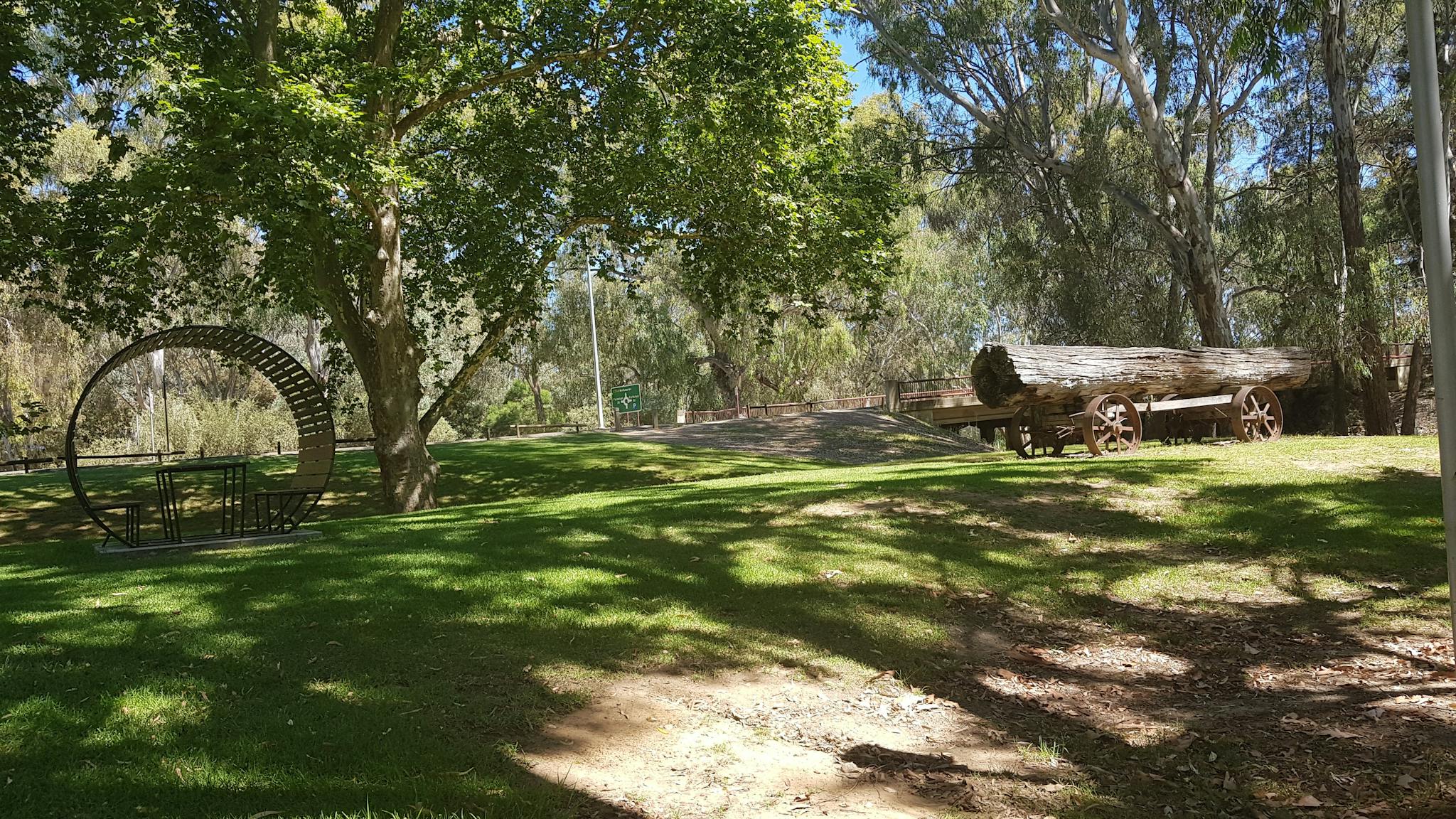 green grass, leafy tree, seating post, large tree trunk on vintage cart, gum trees