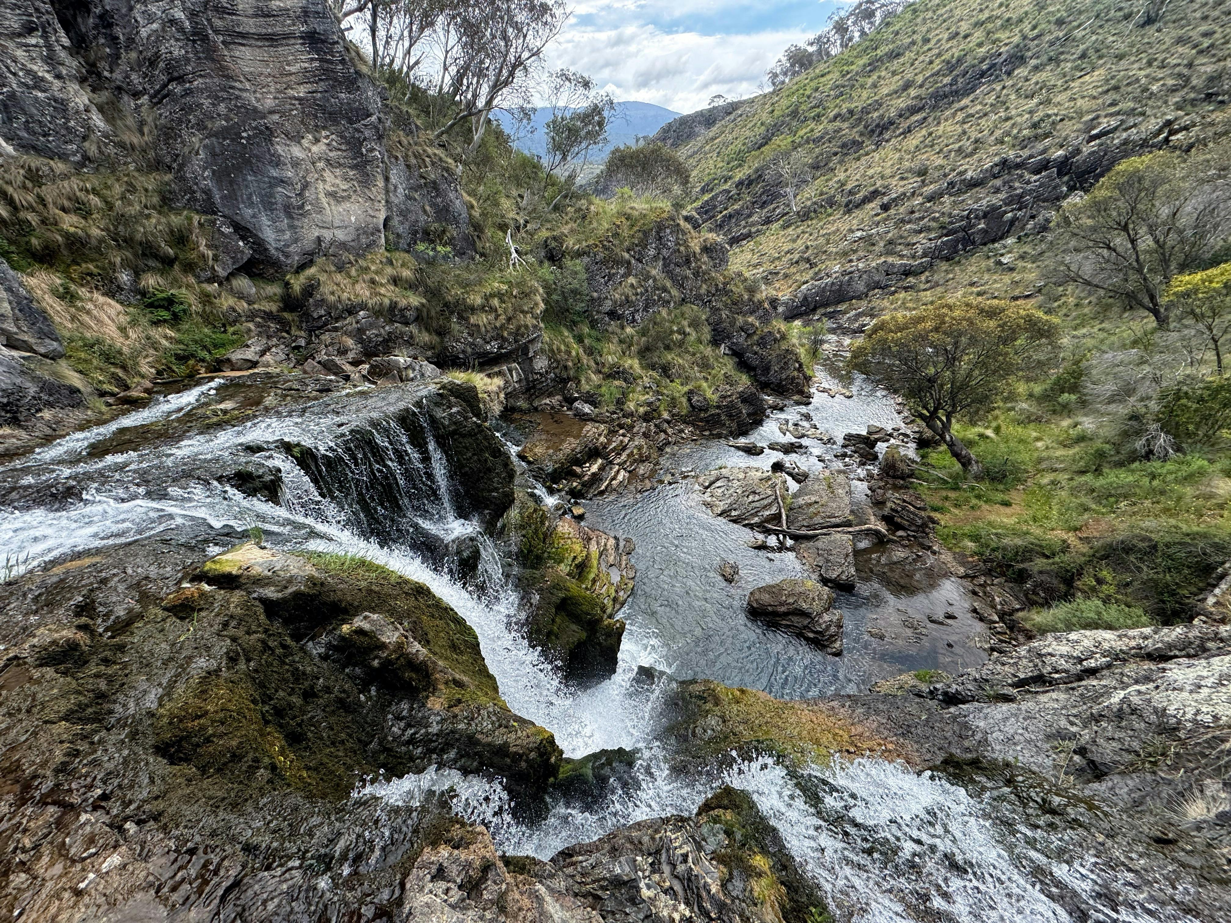 The top of a waterfall leaving into a pool of water with some rocks.