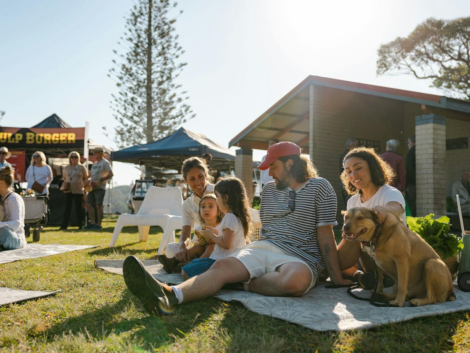 Image of a family sitting on a picnic blanket surrounded by the market stalls