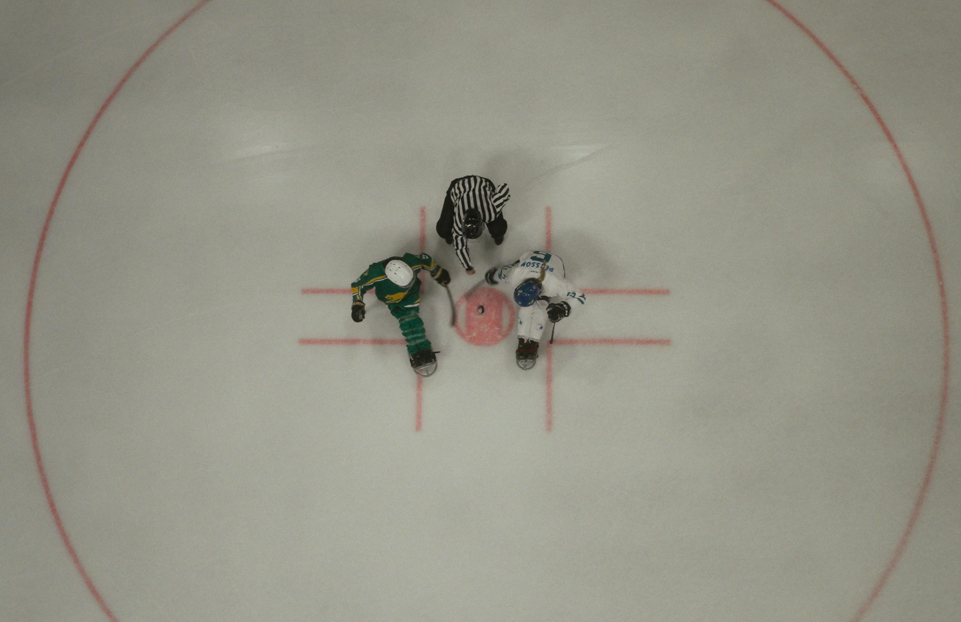 a birds eye view of the hockey puck being dropped by the referee to captains at the start of a game