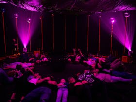 Children lying underneath a billowing parachute in a dark room lit with pink light