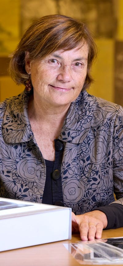 A woman with brown hair is seated at a table, looking directly at the camera.