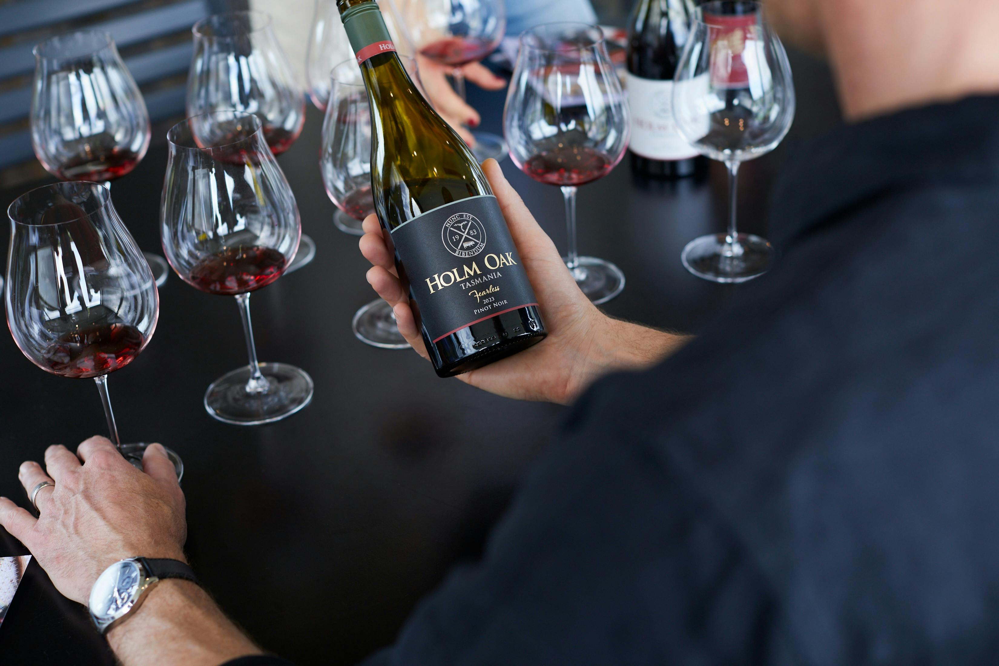 Man holding bottle of Fearless Pinot Noir with glasses of wine in the background
