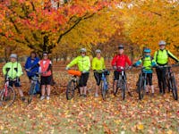 Cyclists and their bikes in front of an orchard  with brilliant yellow and orange leaves