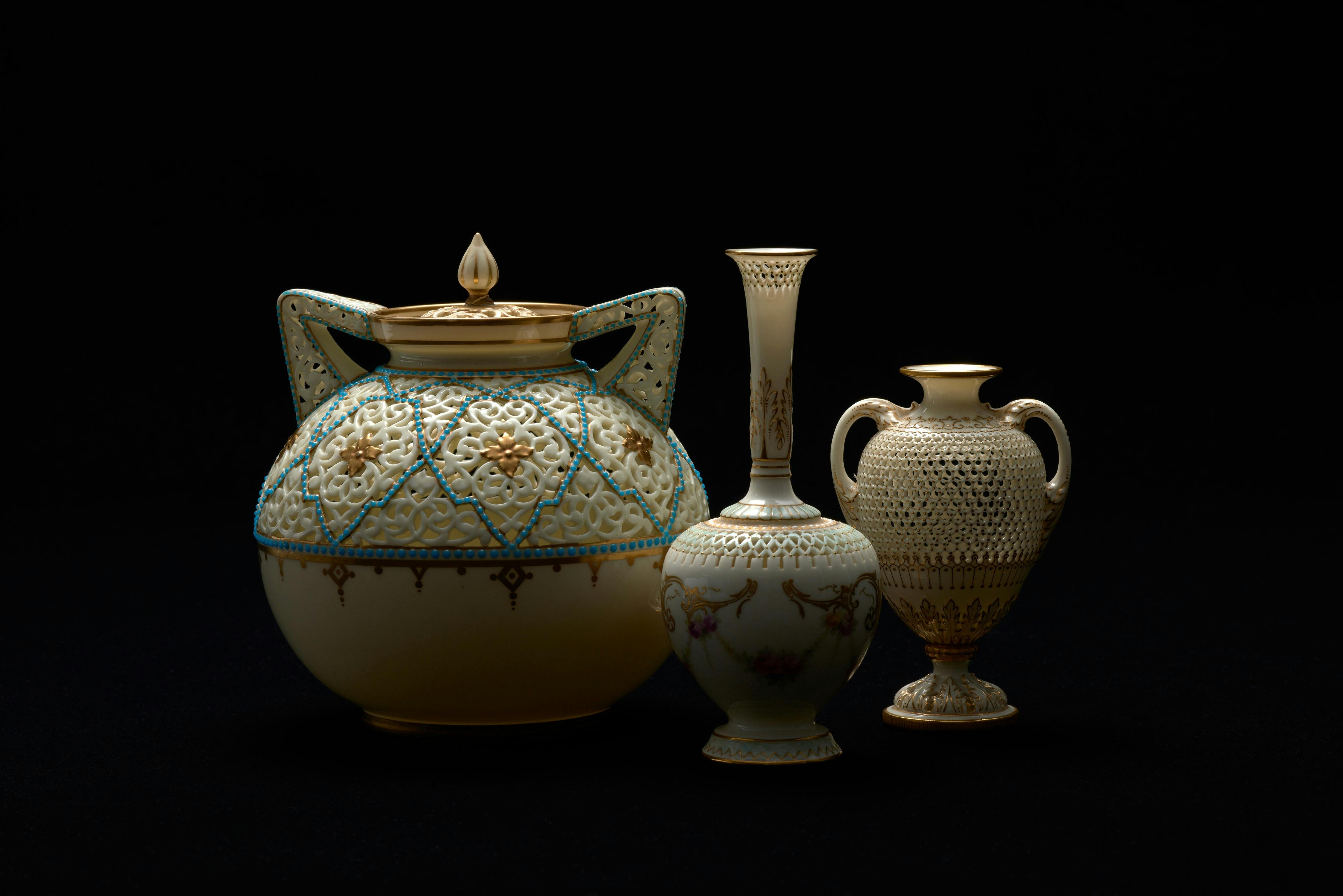 A spotlight illuminates three delicate vases and urns with gold gilt detail