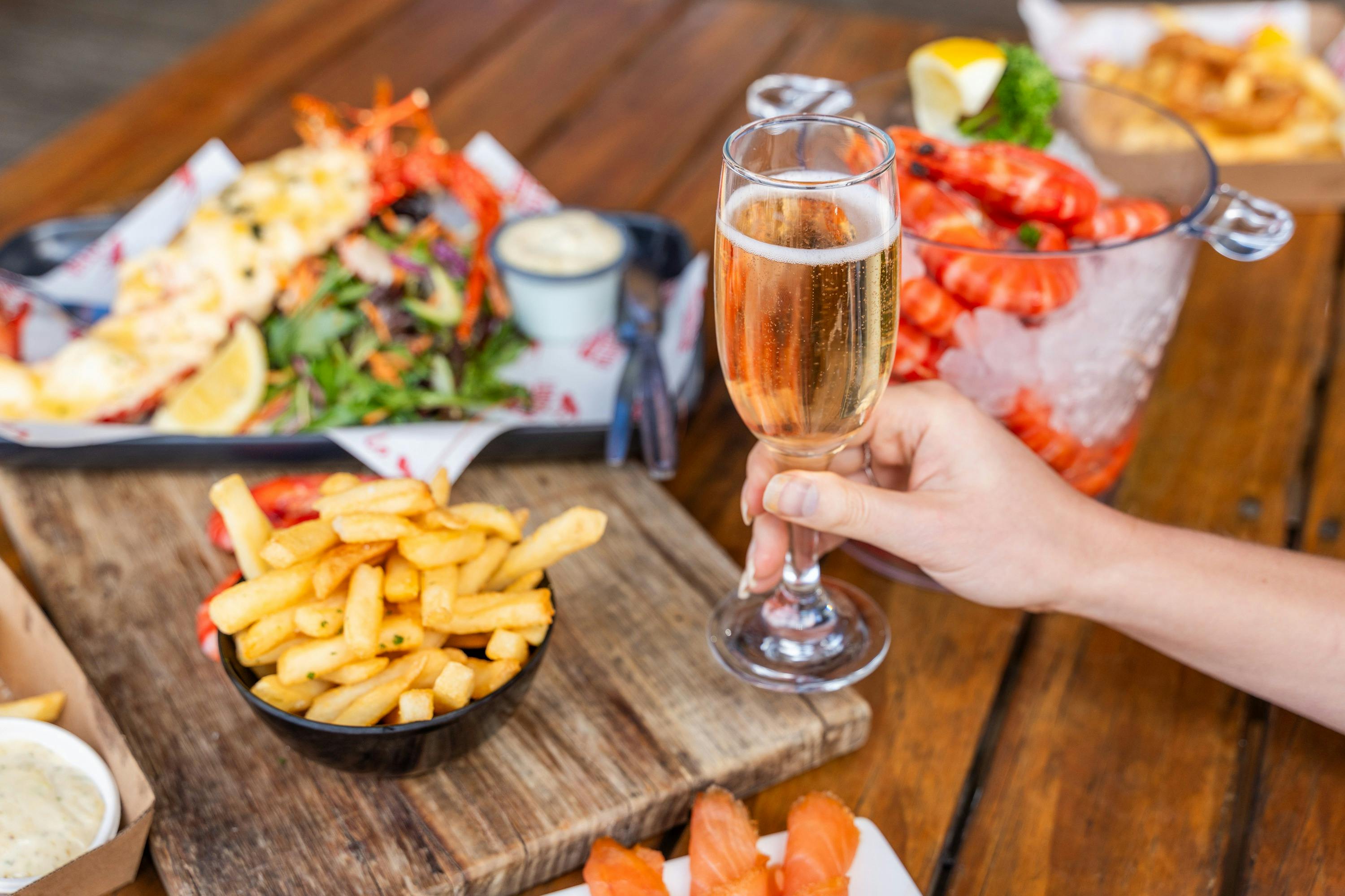Photo of a seafood feast on a table with a customer holding a glass of sparkling wine