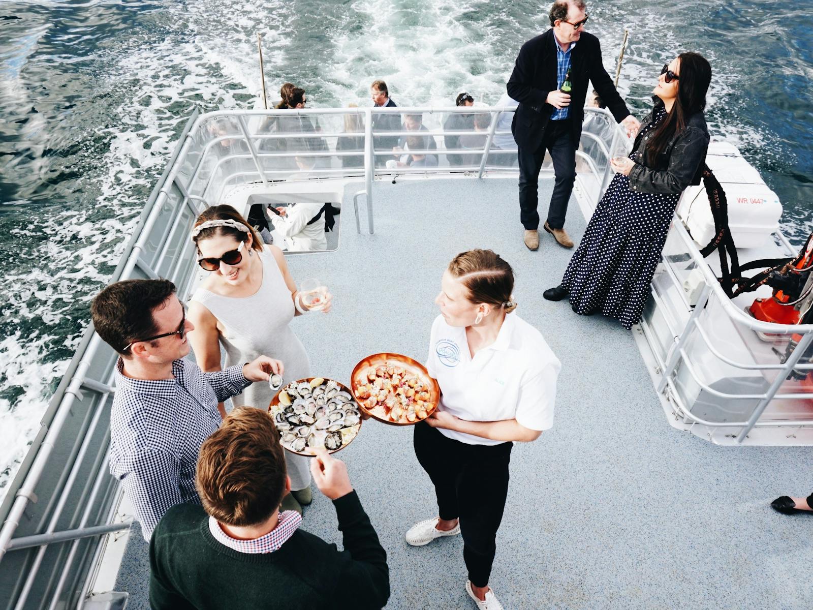 3 people being served canapes by staff on outside deck of vessel.