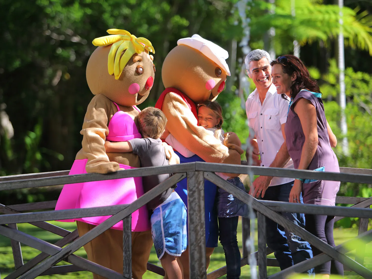 two gingerbread characters hugging kids, with their parents laughing next to them