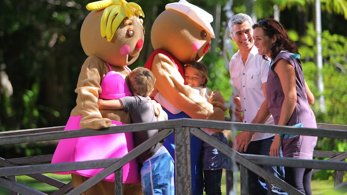 two gingerbread characters hugging kids, with their parents laughing next to them