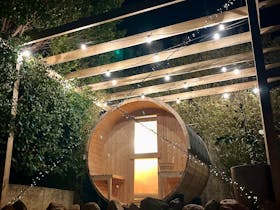 “Wooden barrel sauna with outdoor shower in a coastal garden setting, perfect for relaxation.”