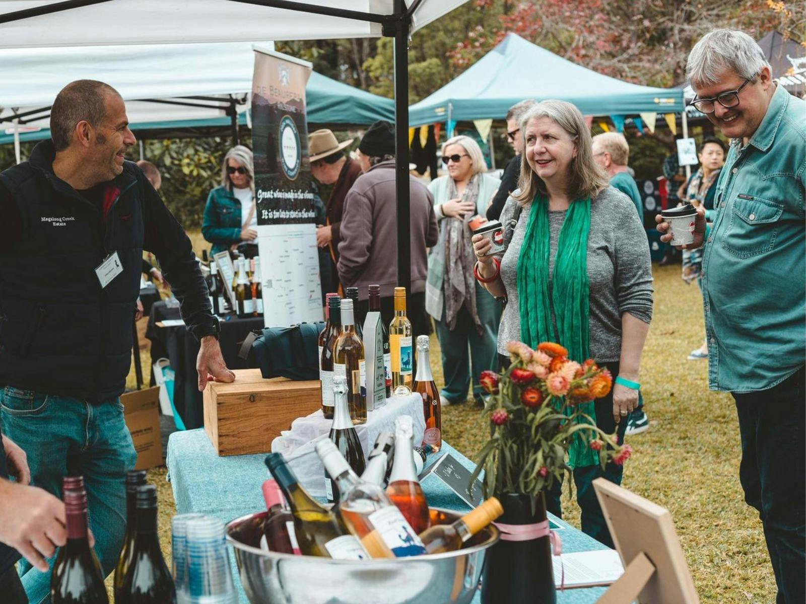A male and female browse a stall. A cooler full of wine bottles sits in the foreground.