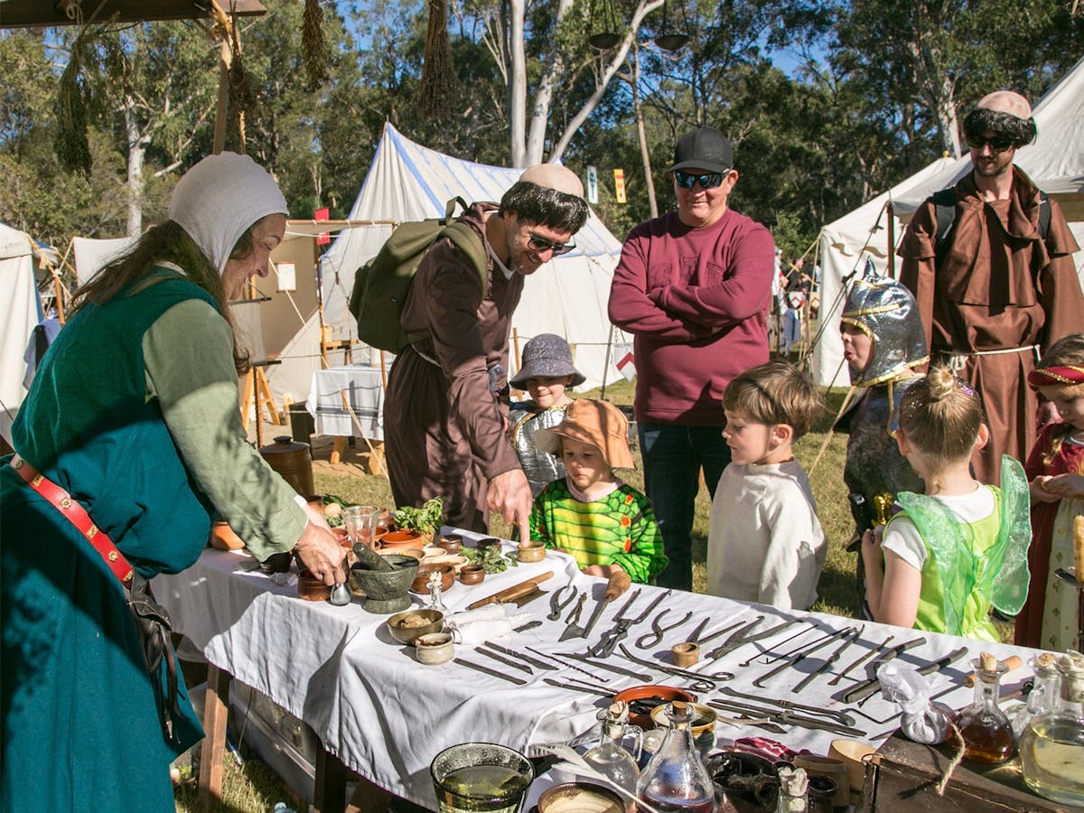 Children and Adults observing a medieval display of herbs and equipment.