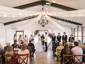 Small indoor wedding setup, with fairy lights, drapes, lots of white & timber