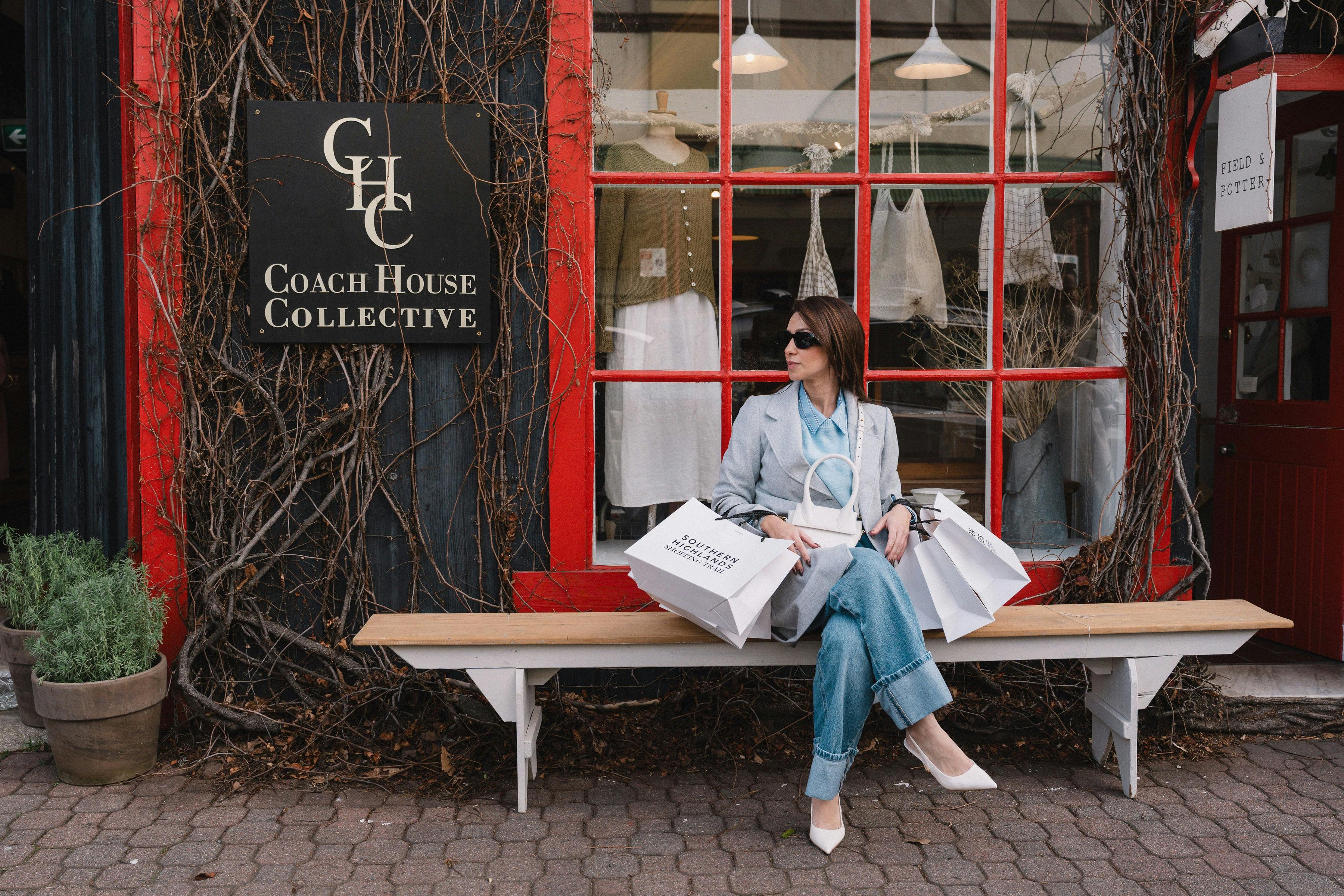 A stylish woman sits on a bench outside Coach House Collective in Bowral holding shopping bags