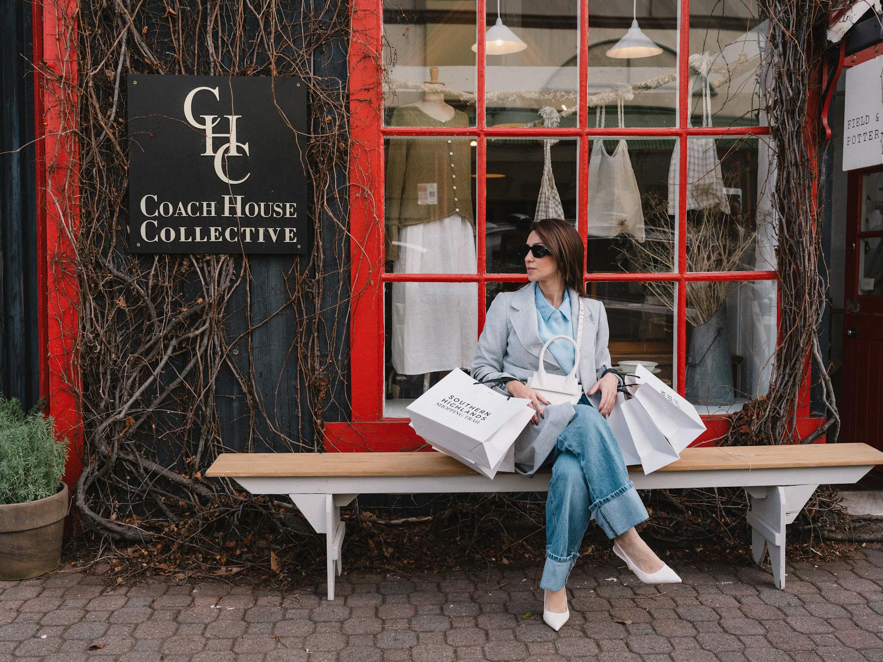 A stylish woman sits on a bench outside Coach House Collective in Bowral holding shopping bags