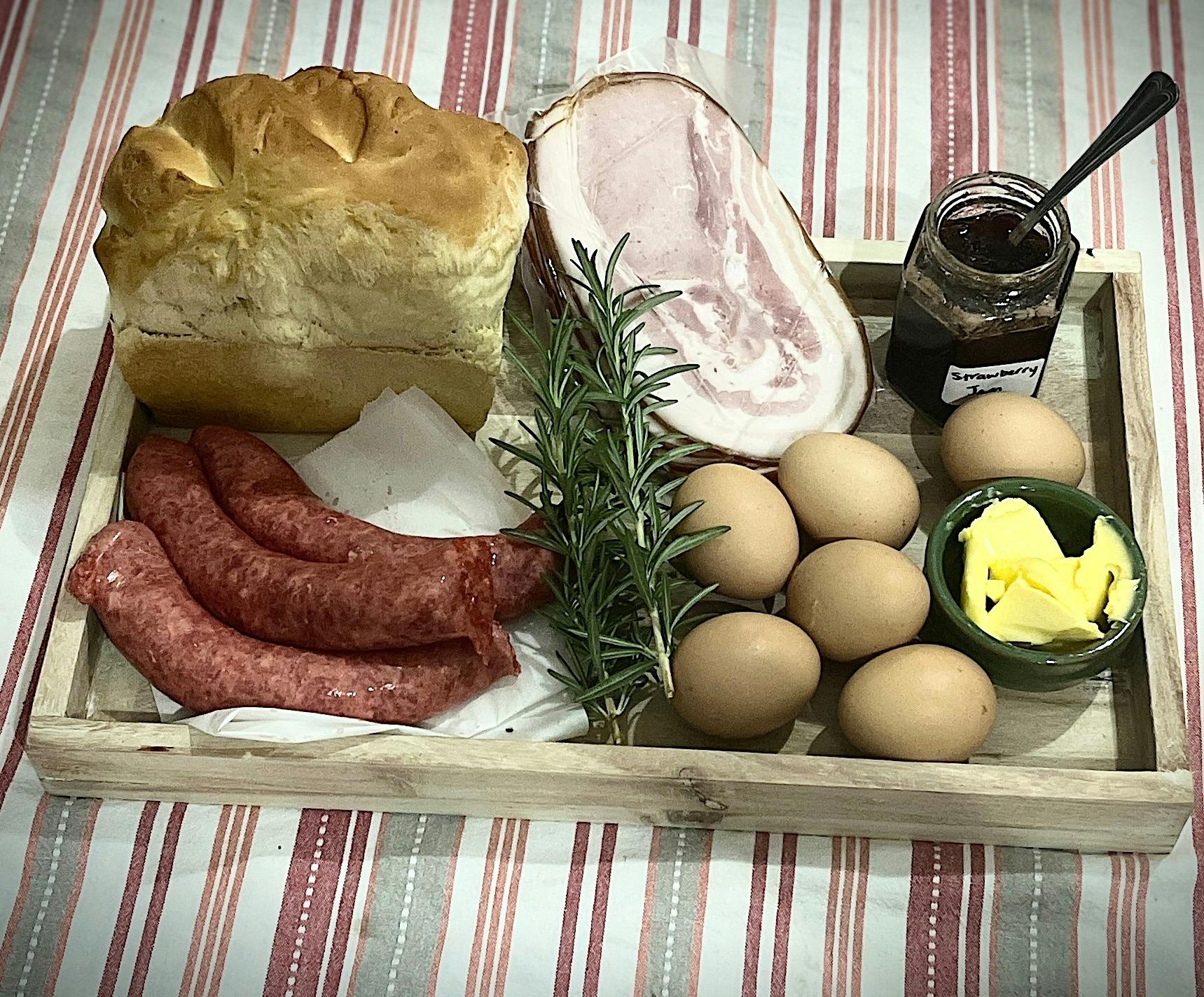Wooden platter of brekky ingredients: gourmet sausages local bacon homemade bread & jam butter eggs
