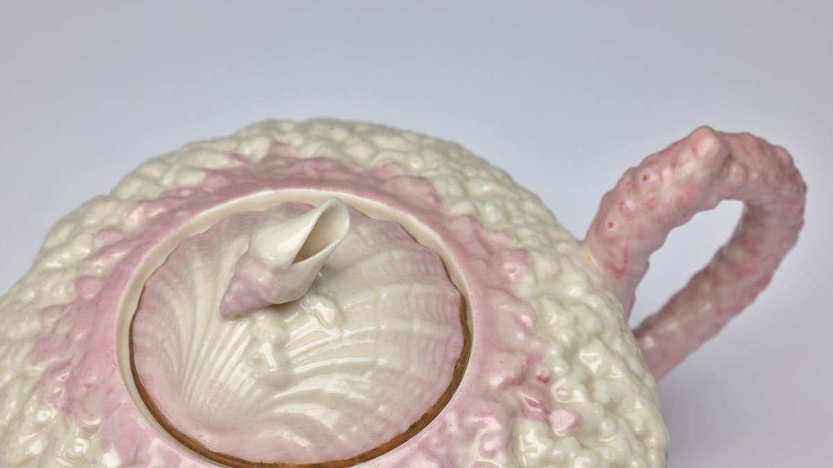 Close up detail of a delicate teapot in cream and pink with intcricate texture