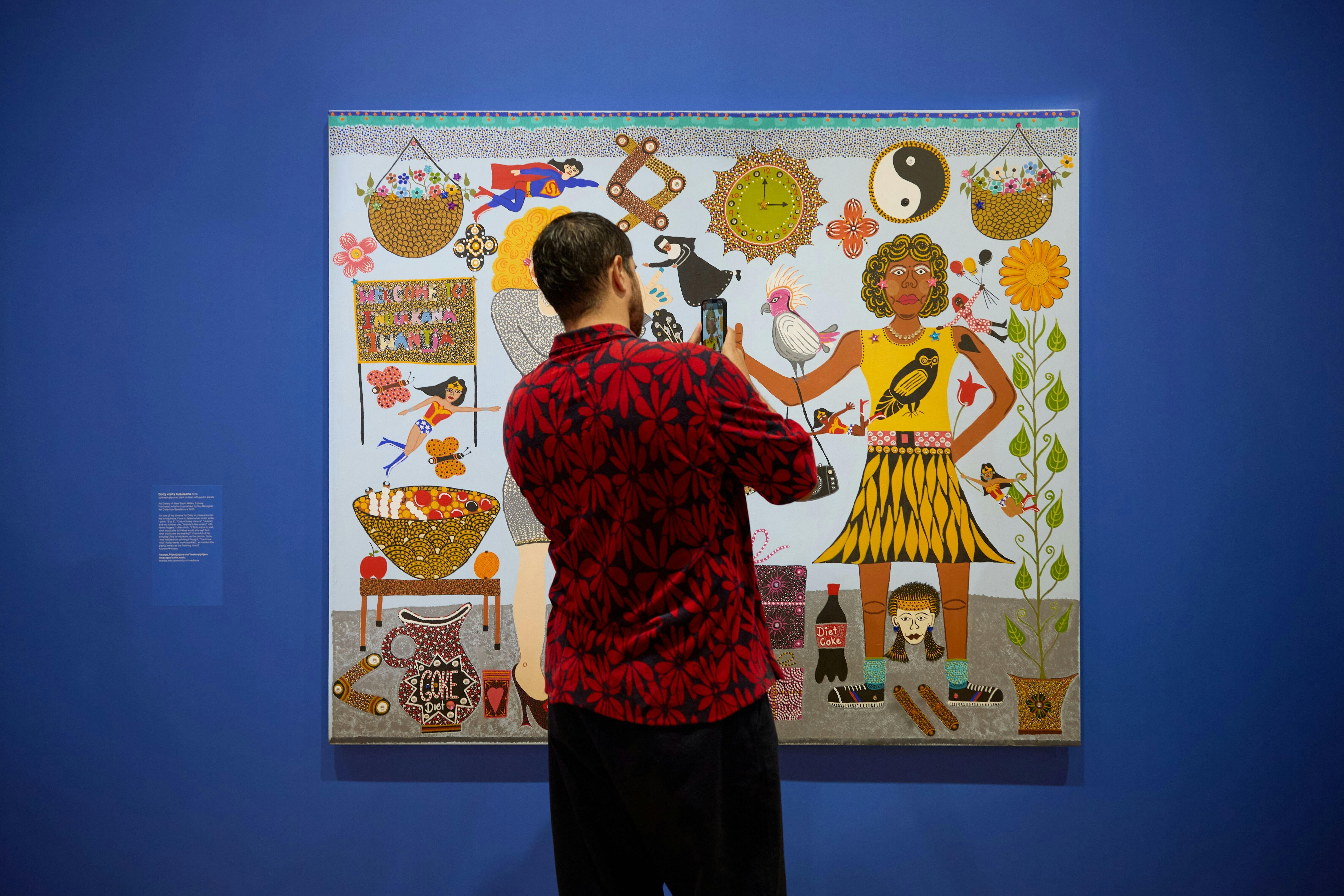 A person in a floral shirt takes a photo of a colourful portrait of Kaylene Whiskey and Dolly Parton