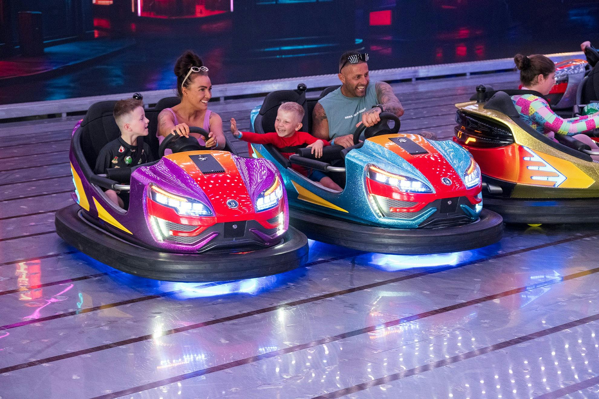 A family of two grown ups and two children happily riding two bumper cars