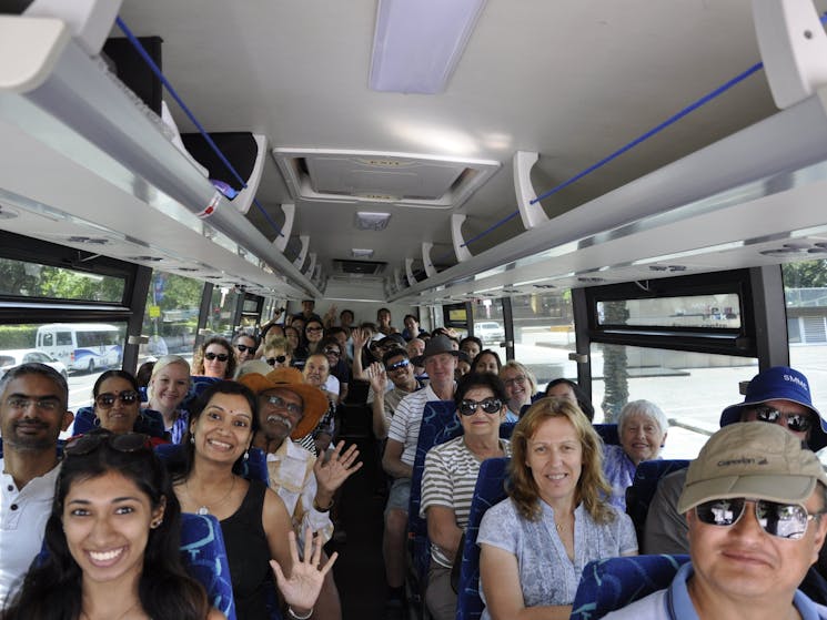 Sydney Sightseeing Bus tour. A group of tourists on the bus smiling and waving.