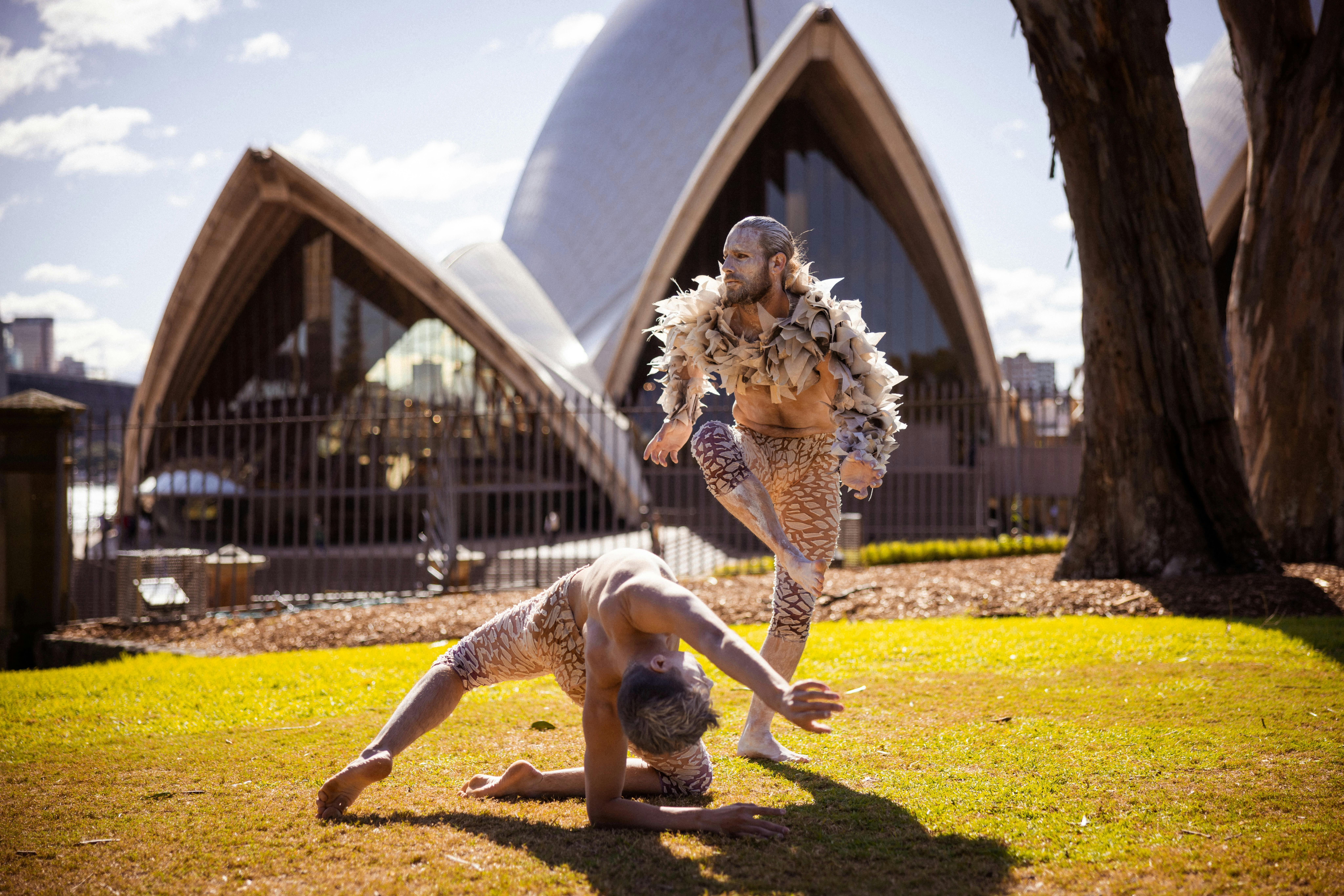Two male dancers pose on the grass outside Sydney Opera House