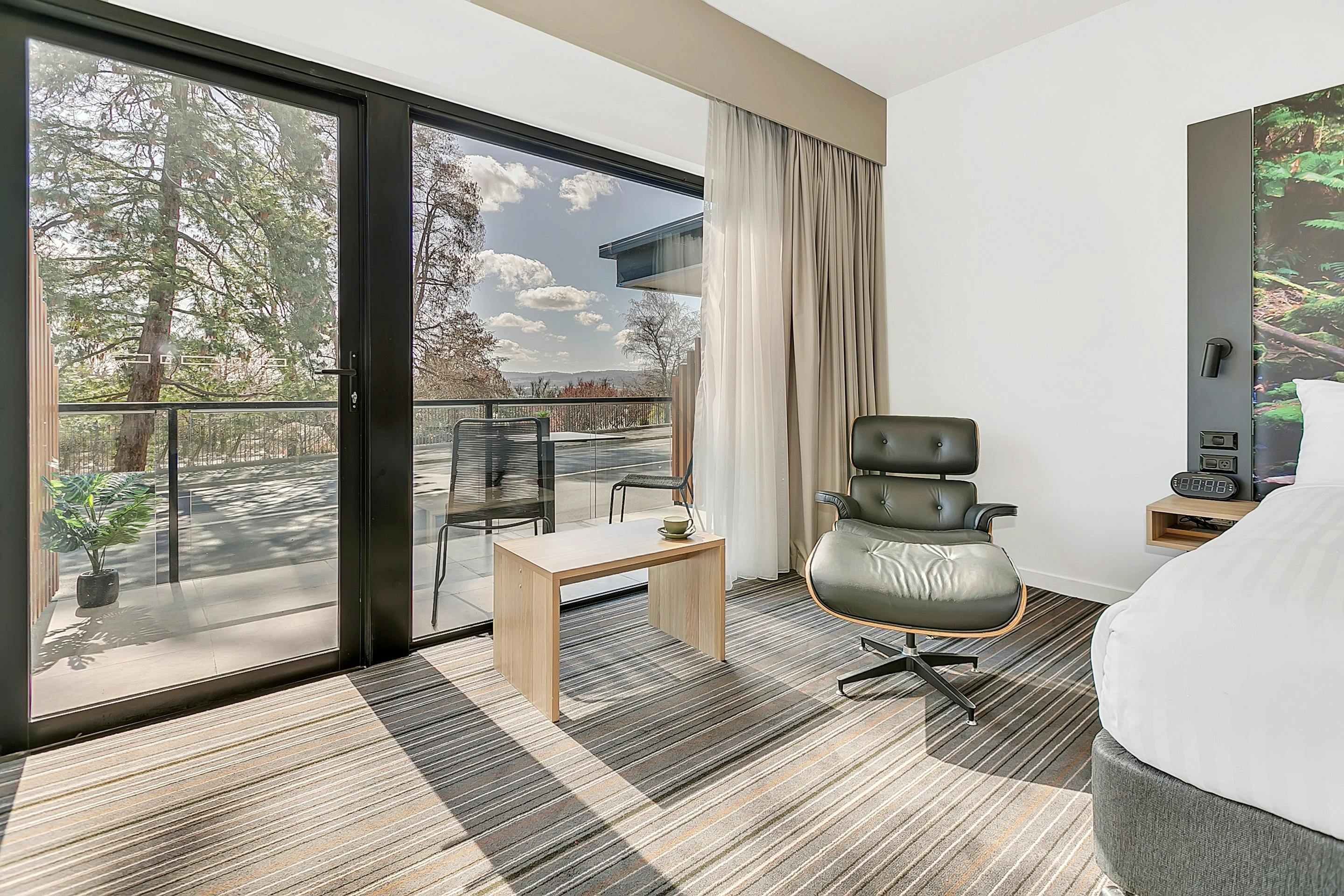 Guest accommodation room, chair and footstool, coffee table, large window to balcony and view.
