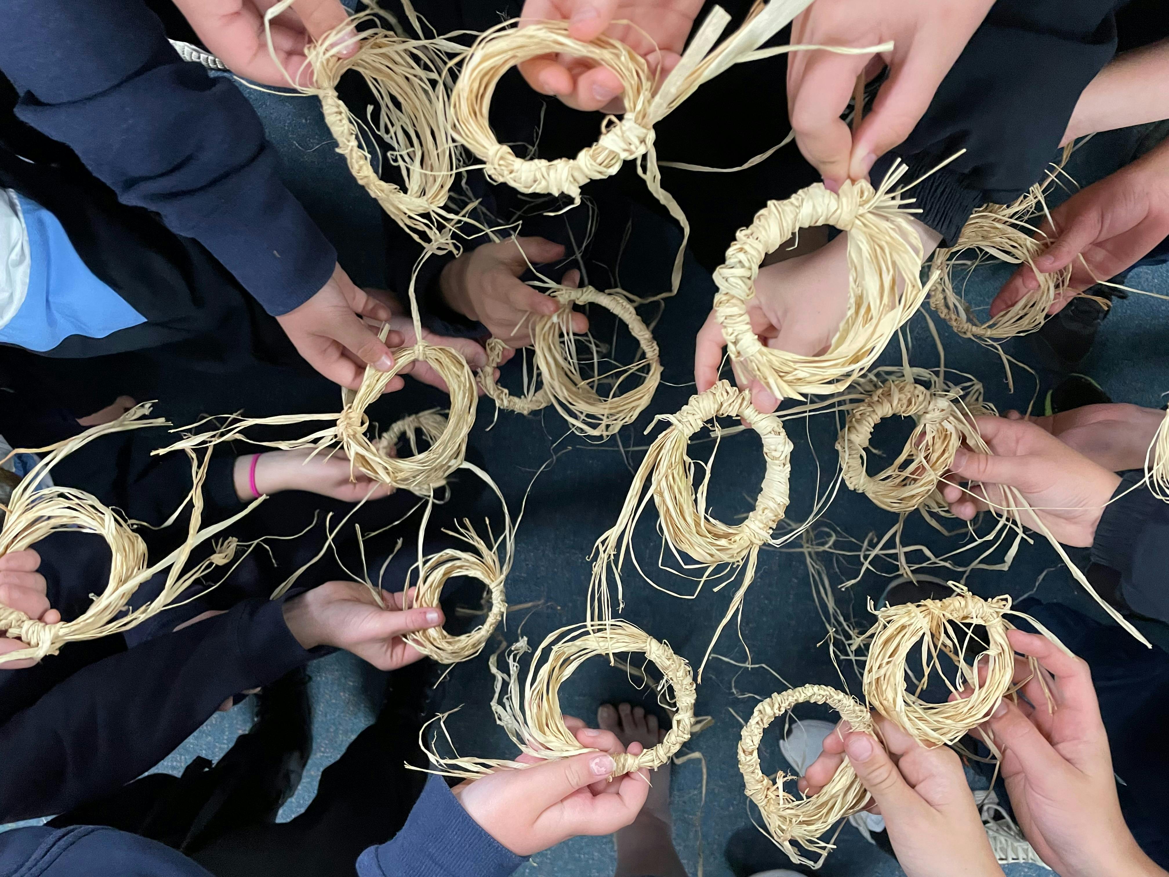 a number of small hands hold rings they have woven from raffia.