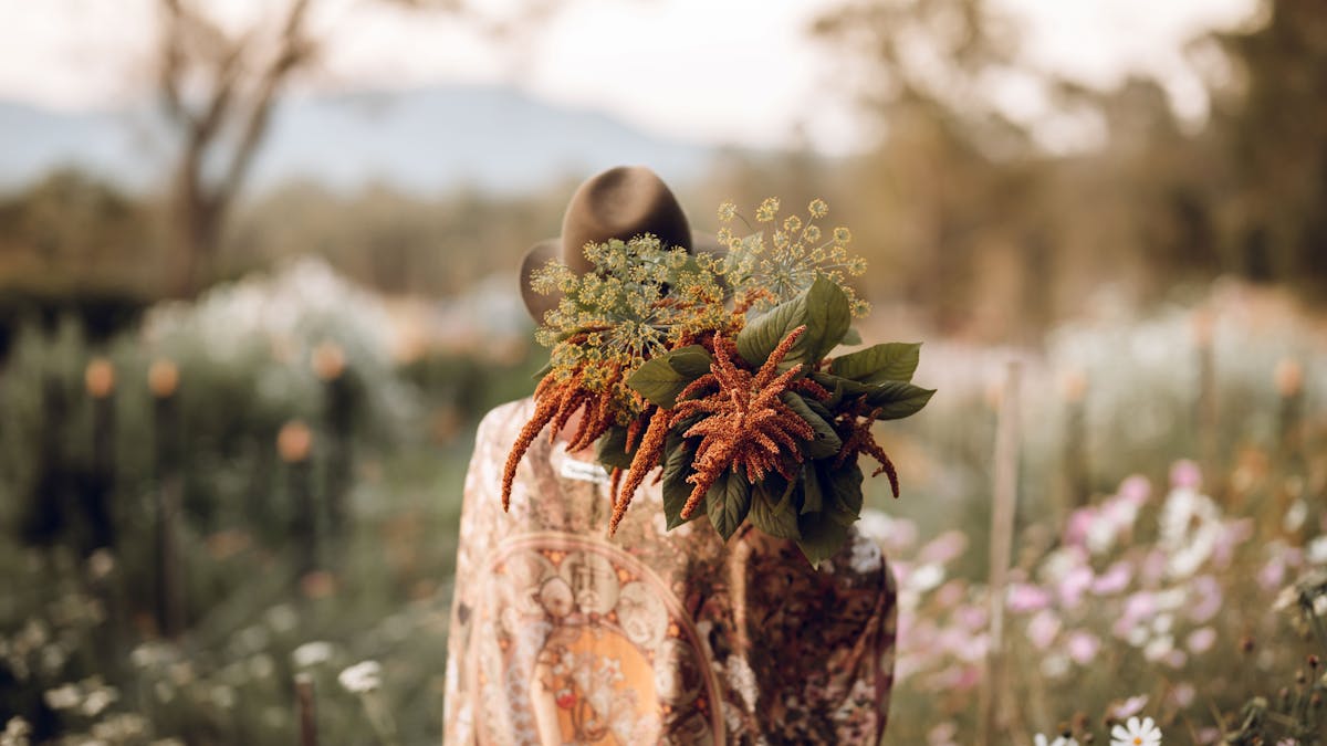 Back of female holding cut flowers in flower field at sunset