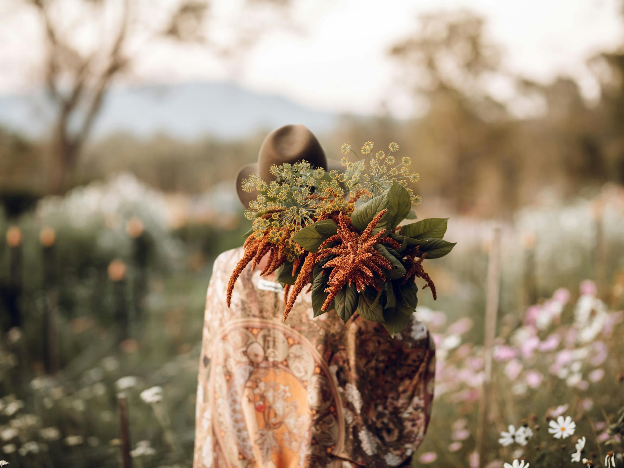 Back of female holding cut flowers in flower field at sunset Back of female holding cut flowers in flower field at sunset