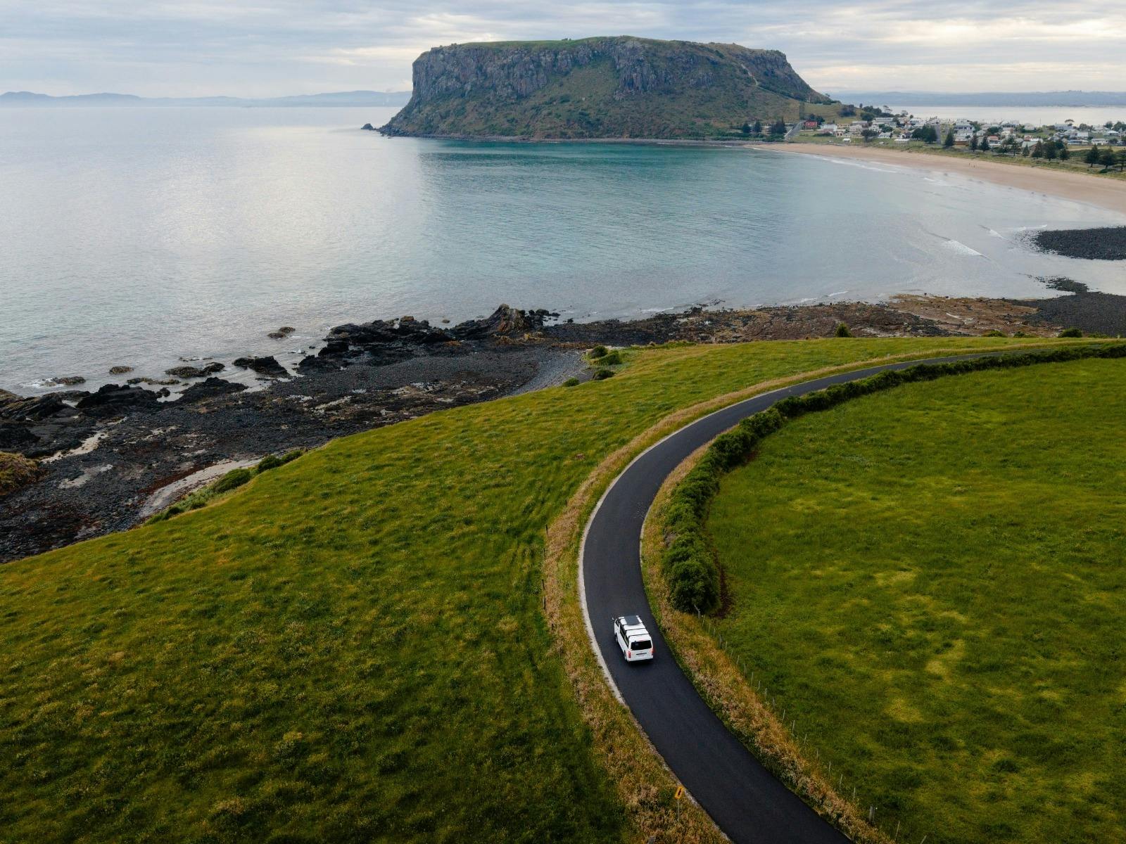 A vehicle drives along a winding road toward a mountain town in the distan